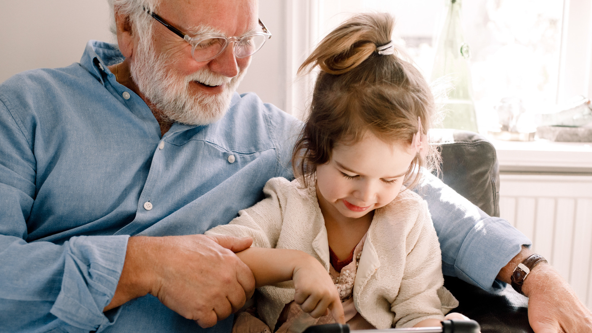 Bestefar sitter med et barnebarn i armkroken og ser på Ipad.